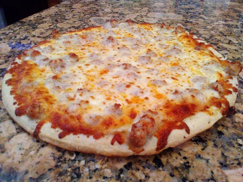 Photo of a pizza with sausage visible under the melted cheese.