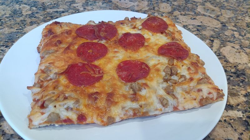 Photo of a rectangular pepperoni and sausage pizza.