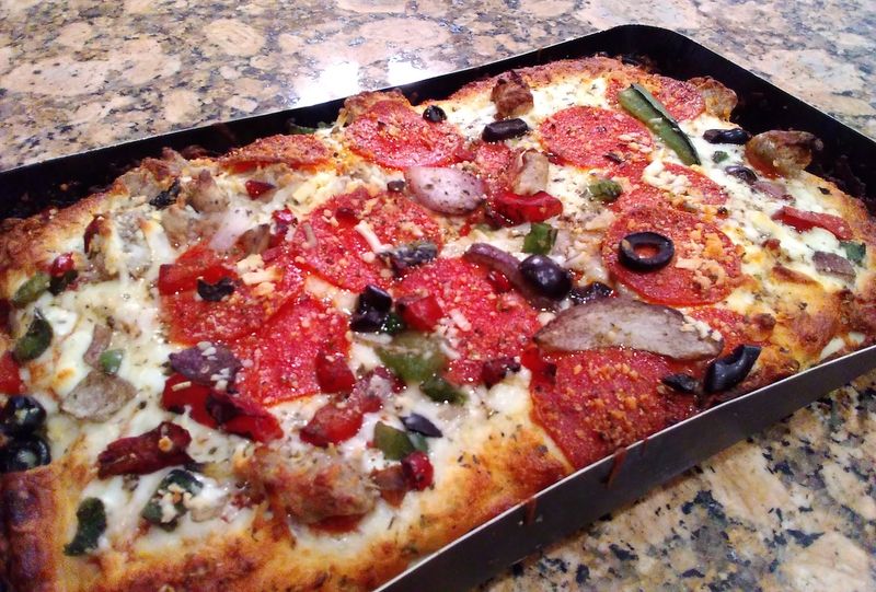 Photo of a deep dish supreme pizza in a paperboard baking tray.