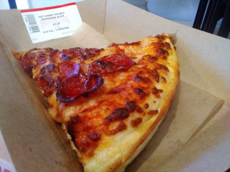 Photo of a slice of hot honey double pepperoni pizza on a cardboard tray.